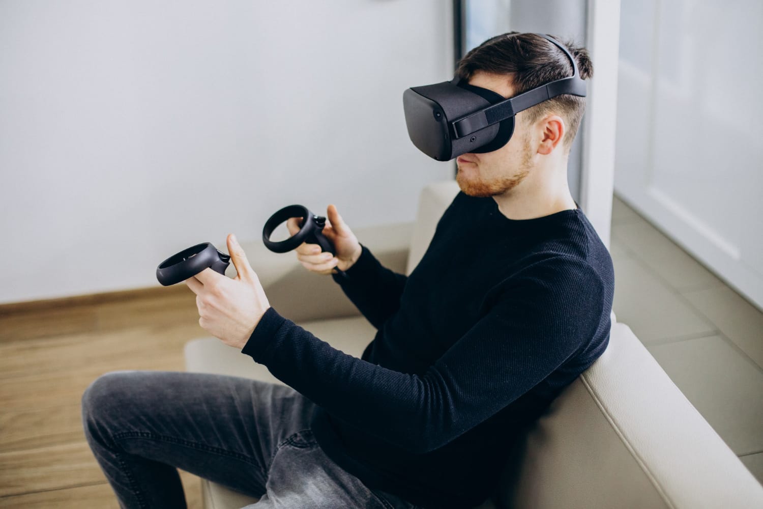 A man sitting on a couch wearing a VR headset and using VR controls.